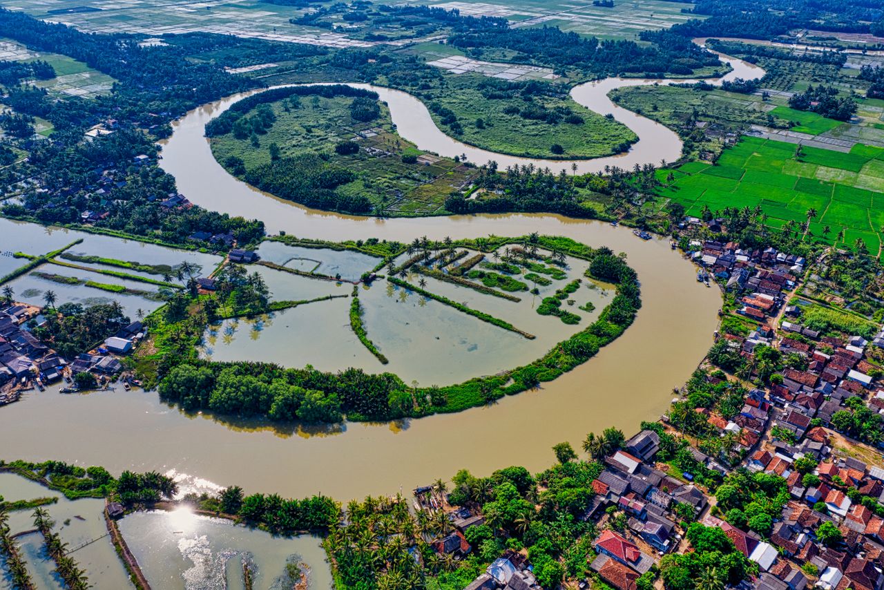 Aerial view capturing the vibrant landscape of a meandering river surrounded by green fields and houses.